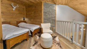 A cabin with two wooden beds, a stone wall, a white chair, and a balcony with a railing. - 40m from ski slopes, 2nd floor, fitness, swimming pool, sauna, balcony, fireplace or stove, tv (Les Orres)