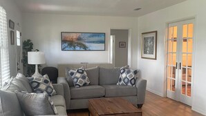 Ein modernes Wohnzimmer mit einem grauen Ecksofa, zwei Holztischen und einem großen Gemälde an der Wand.