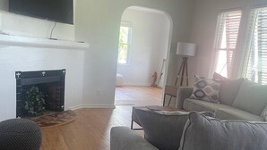Ein Wohnzimmer mit grauem Sofa, Kamin, Fernseher darüber und Holzboden.