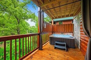 Une terrasse en bois avec un jacuzzi et un petit banc, entourée d’une rambarde en bois et d’un mur de pierres.