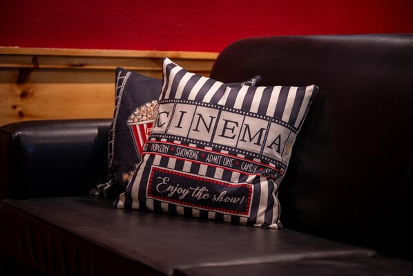 Un coussin sur le thème du cinéma, posé sur un canapé en cuir foncé, avec du texte imprimé dessus.