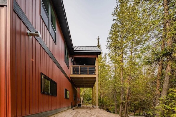 Un bâtiment moderne à la façade rouge, doté d’un balcon, avec une zone boisée en arrière-plan.