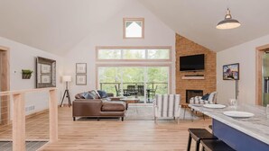 A spacious living area with a large window, a fireplace, and a dining area with a kitchen counter. - Family Retreat | Game Room + EV Charger (Sturgeon Bay)