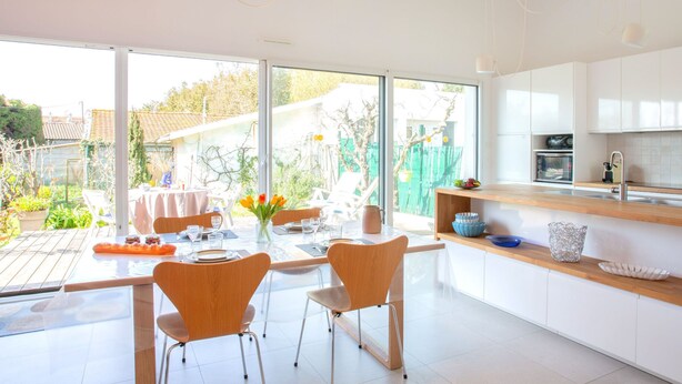 Une cuisine moderne dotée d’un grand îlot central, de meubles blancs et d’un coin repas avec une table dressée pour deux personnes.