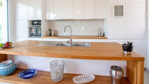 Une cuisine moderne avec des meubles blancs, un plan de travail en bois, un évier en acier inoxydable et un four encastré.