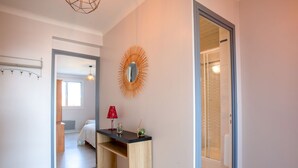 A modern bedroom with a bed, a bedside table, and a mirror. There is a door leading to another room.