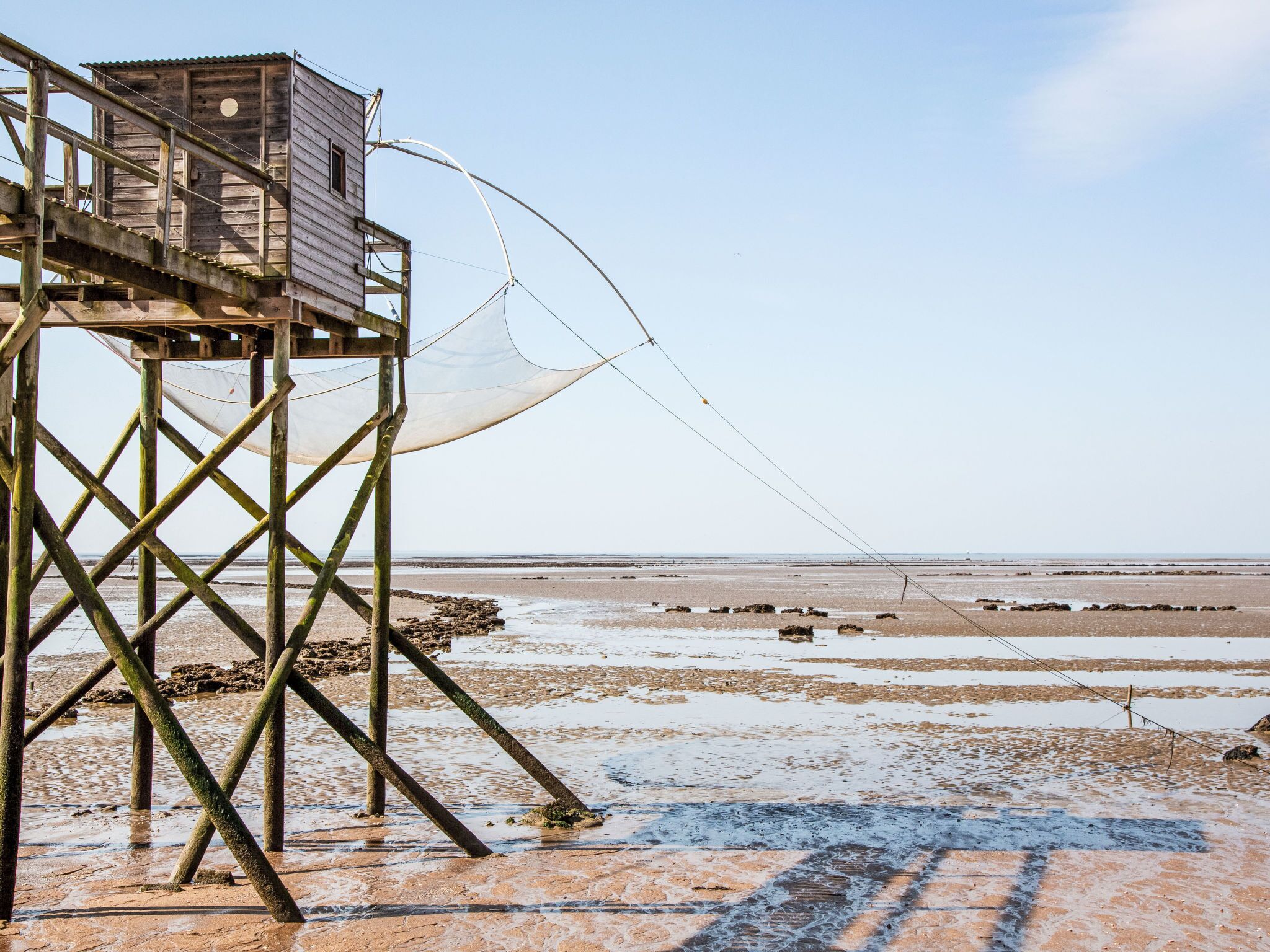 Een houten constructie met een platform, mogelijk een uitkijkpunt, met uitzicht op een strand onder een heldere lucht.