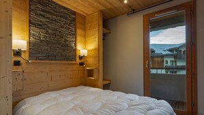 A bedroom with a large bed, wooden walls, stone accents, and a view through a glass door. - 40m from ski slopes, 2nd floor, fitness, swimming pool, sauna, tv, ski locker, 56m², Les Orres (Les Orres)