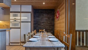 Comedor con una mesa de madera dispuesta para seis personas, rodeada de sillas. Se observa una pared de piedra y un techo de madera.