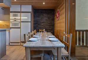 A dining area with a wooden table set for six, surrounded by chairs. A stone wall and a wooden ceiling are visible. - 40m from ski slopes, 2nd floor, fitness, swimming pool, sauna, tv, ski locker, 56m², Les Orres (Les Orres)