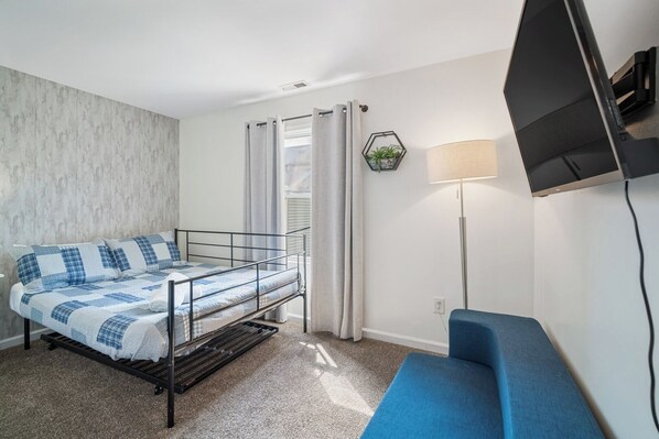 A compact room with a metal bunk bed, a blue sofa, a floor lamp, and a mounted TV.