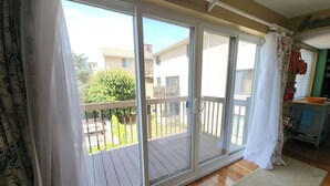 Una habitación con puerta de vidrio corrediza que da a una terraza de madera, una alfombra pequeña y una cocina con carrito.