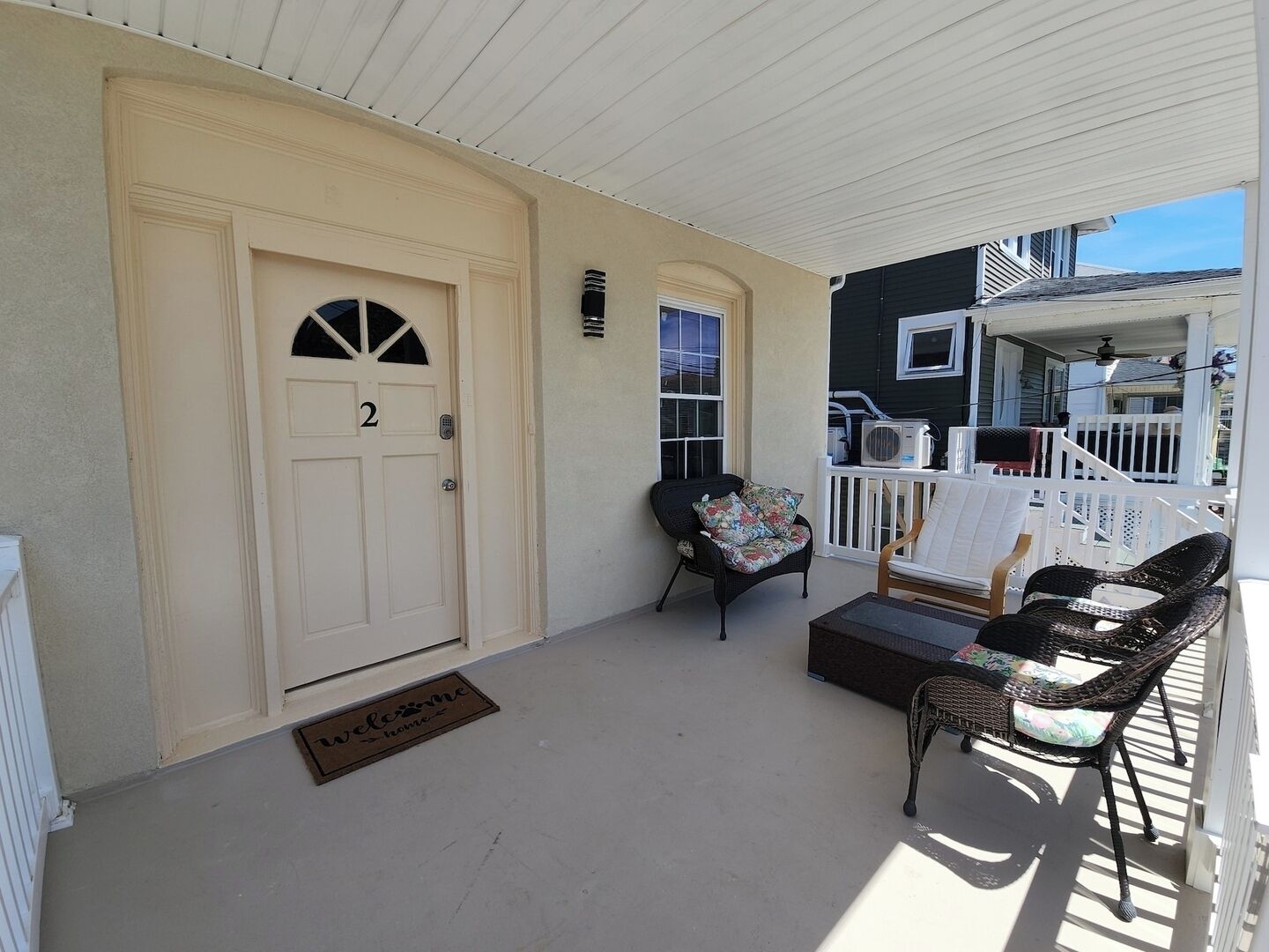 A covered porch with a white door marked '2', a welcome mat, and wicker furniture.