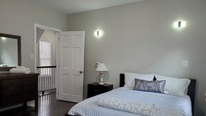 Een slaapkamer met een bed, een dressoir, een nachtkastje, een spiegel en een deur.