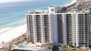 Un hotel de gran altura con múltiples balcones, una zona de piscina y vistas a la playa.