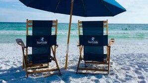 Dos sillas de playa con una sombrilla azul, identificadas con el letrero "Surfside Resort", mirando hacia el océano.