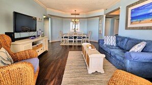 Una sala de estar con televisor, muebles de mimbre, un sofá azul y un comedor con candelabro.