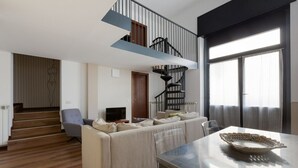Una sala moderna con sofá, una mesa de comedor con un cuenco decorativo, una escalera y una televisión.