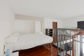 Une chambre à coucher avec un lit, un plancher en bois, un escalier et un téléviseur.