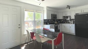 Ett kök med vita skåp, ett svart kylskåp, en mikrovågsugn och en spis. Där finns ett glasbord med röda stolar.