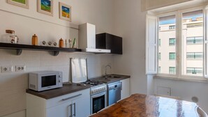 Une cuisine compacte équipée d’un four à micro-ondes, d’une cuisinière et d’un lave-vaisselle, avec un plan de travail en bois et une fenêtre donnant sur des immeubles.