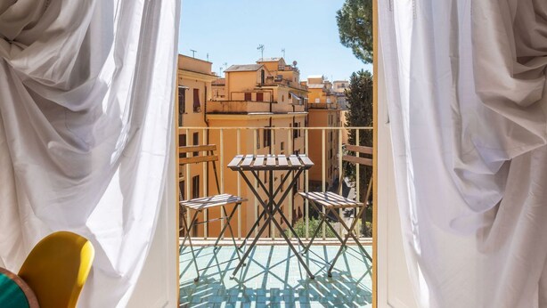 Un balcon avec une table et des chaises, donnant sur un paysage urbain avec des immeubles.