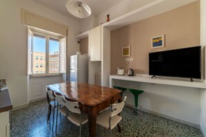Une cuisine de taille réduite comprenant une table à manger, des chaises, un réfrigérateur, un téléviseur et une fenêtre.