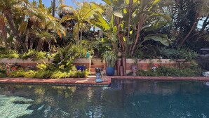 Un espace piscine agrémenté d’une statue de sirène, entouré d’une végétation tropicale luxuriante et d’un mur de pierre.