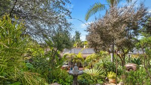 Un jardin luxuriant avec une fontaine en pierre, diverses plantes tropicales et, au fond, un bâtiment de style traditionnel.