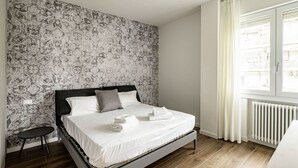 A bedroom with a bed, a small table, a radiator, and a window with curtains. - GuestHost - Modern Santa Rita Apartment - Padova (Padova)
