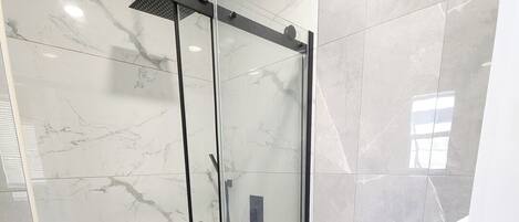 A modern bathroom with a glass-enclosed shower, a white toilet, and a red rug.