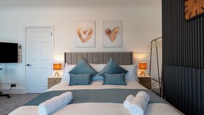 Une chambre bien rangée, avec un lit, deux décorations murales en forme de cœur, une horloge et un téléviseur accroché au mur.