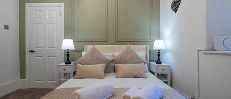 A neatly made bed with two pillows, a bedside lamp, and rolled towels on a beige bedspread.