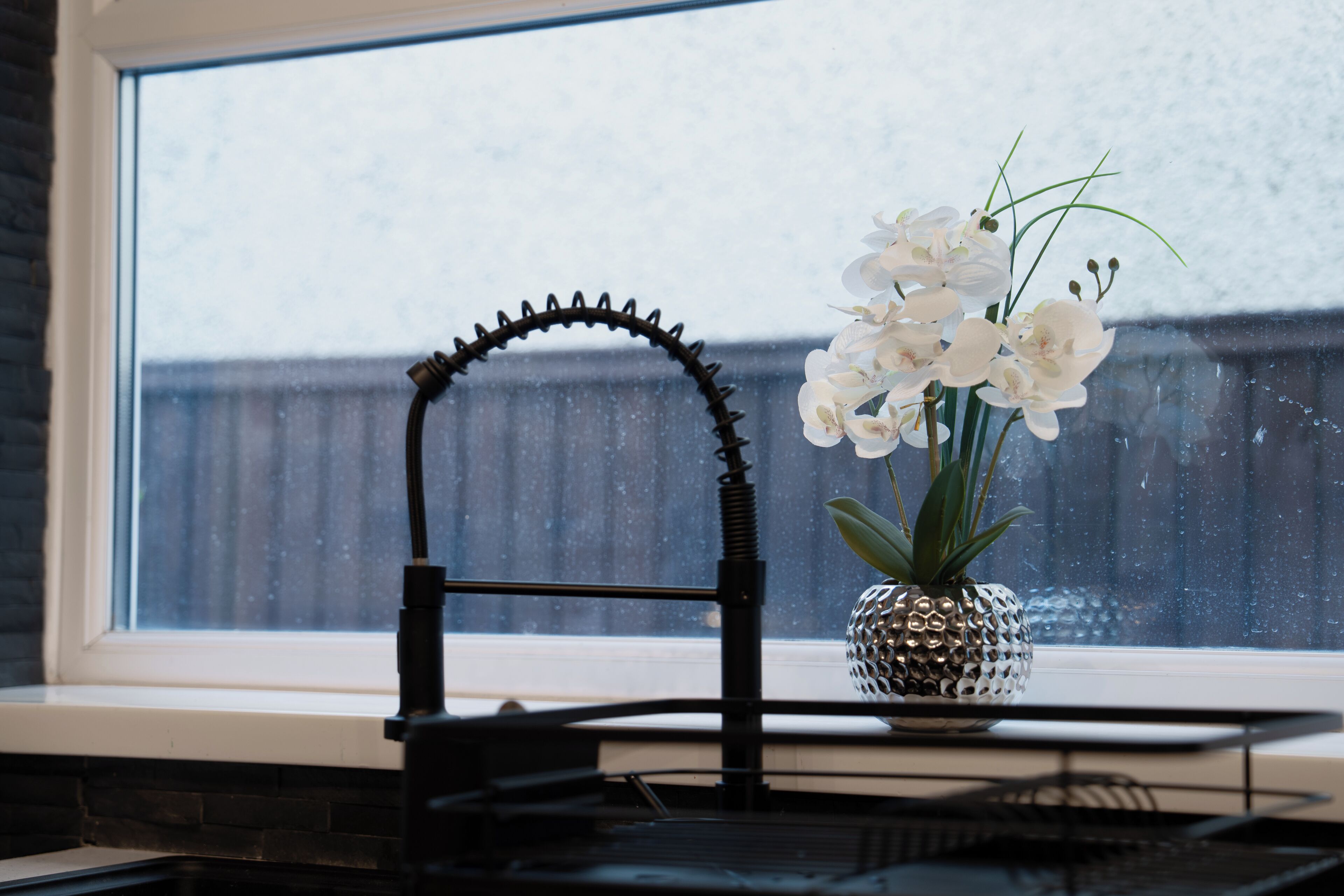 A kitchen window with a decorative black metal frame, a white orchid vase, and a pineapple-shaped pot.
