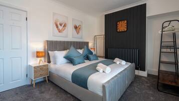 A neatly arranged bedroom with a bed, bedside tables, a wall clock, and a radiator.