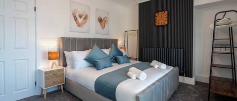 A neatly arranged bedroom with a bed, bedside tables, a wall clock, and a radiator.