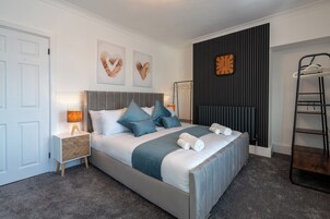 Un dormitorio ordenado con cama, mesitas de noche, un reloj de pared y un radiador.