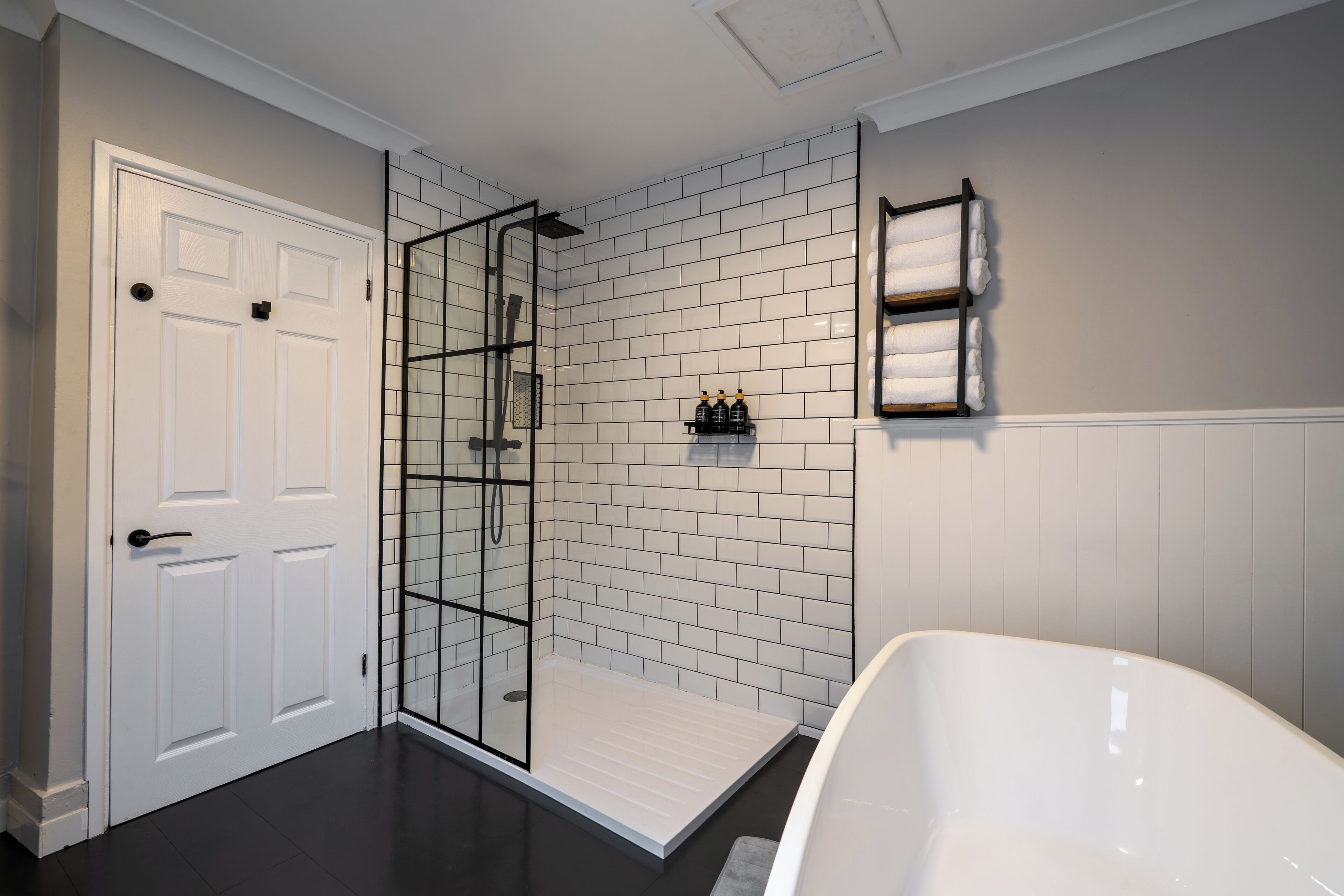 A modern bathroom with a white bathtub, a glass-enclosed shower, and a white tiled wall.