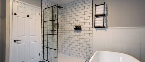 Un bagno moderno con una vasca da bagno bianca, una doccia vetrata e una parete rivestita di piastrelle bianche.