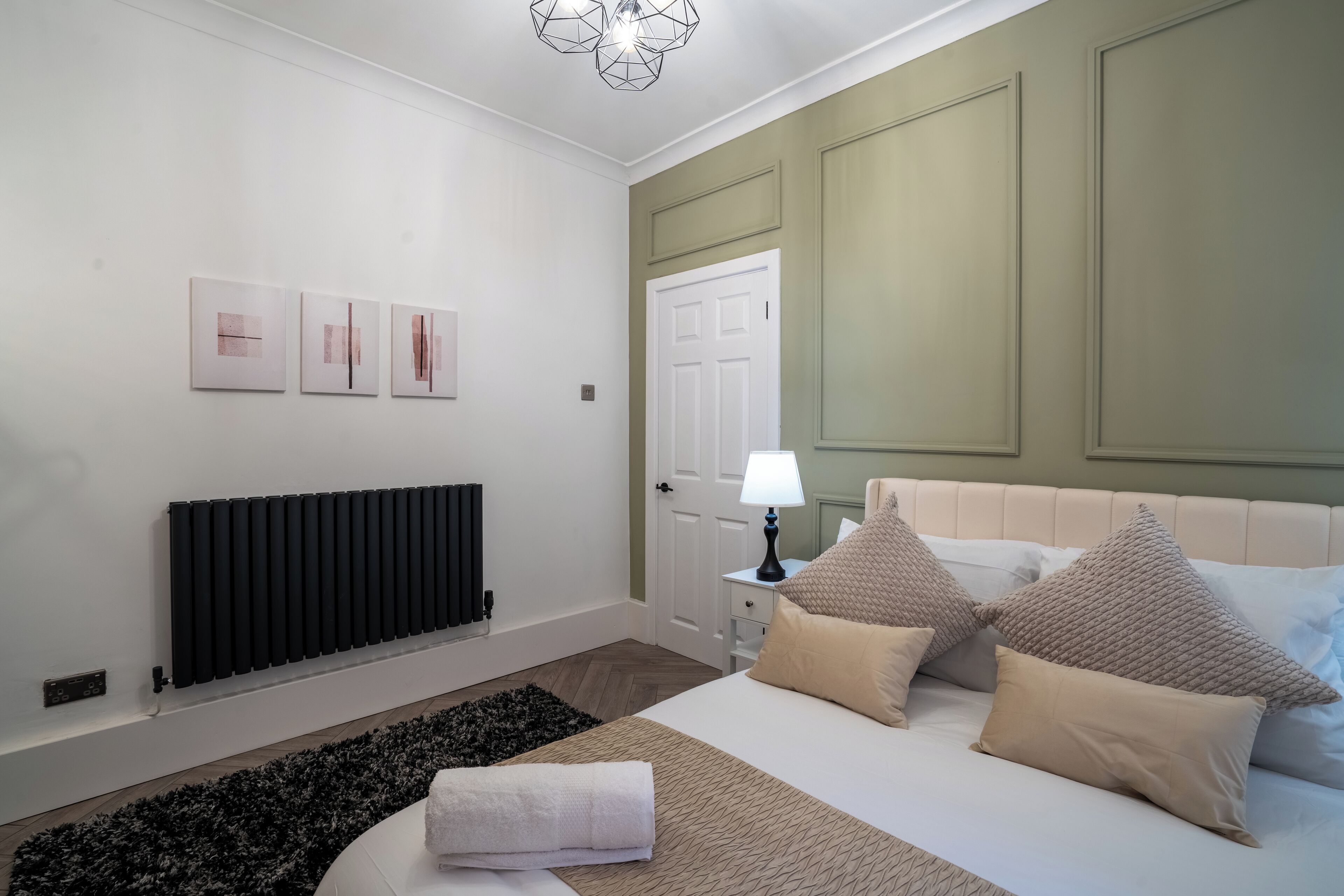 A bedroom with a bed, a radiator, a door, and three framed pictures on the wall.