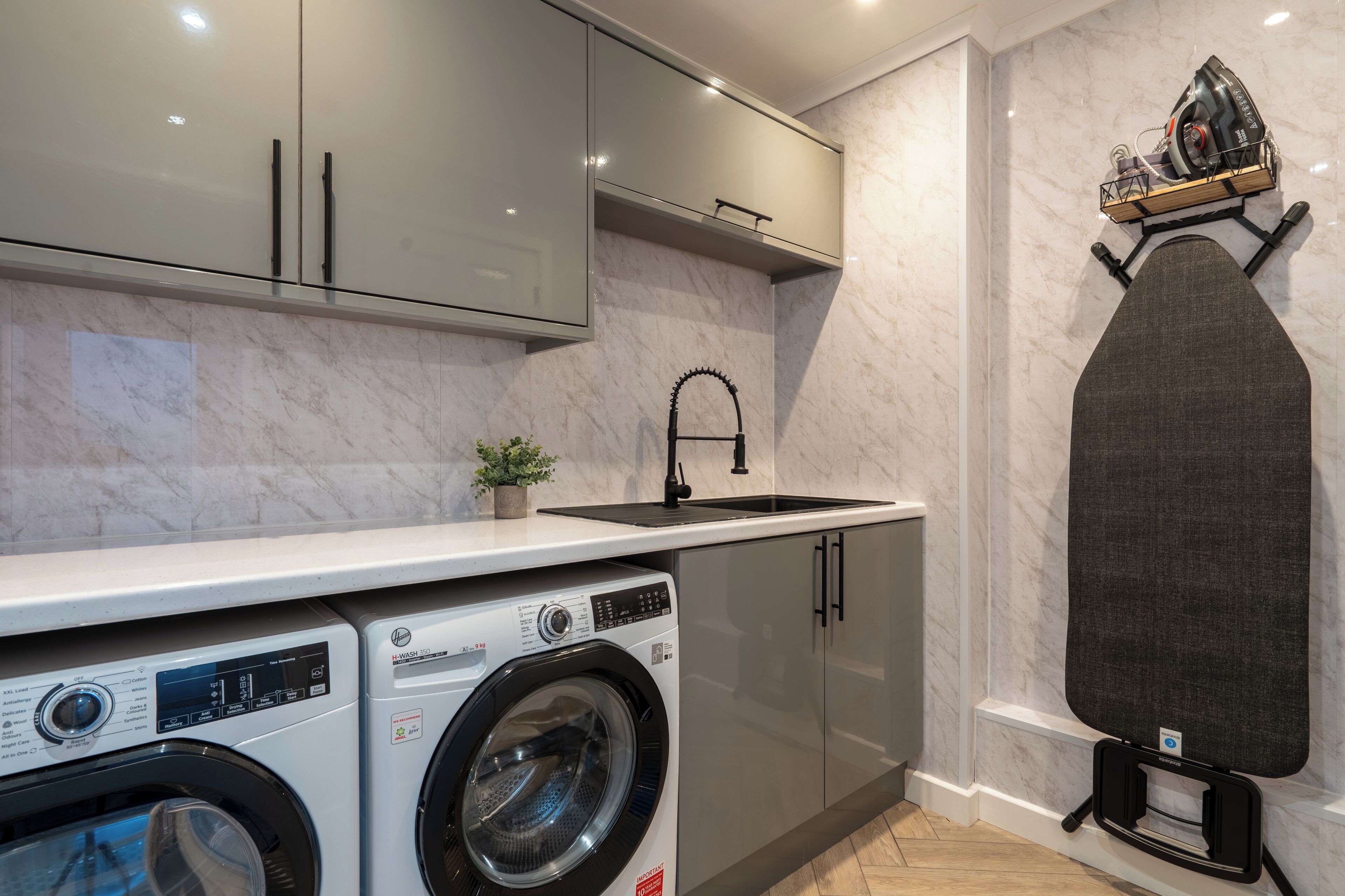 A compact kitchen with a washing machine, a sink, and a built-in ironing board.