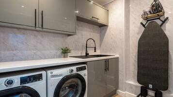 A compact kitchen with a washing machine, a sink, and a built-in ironing board.