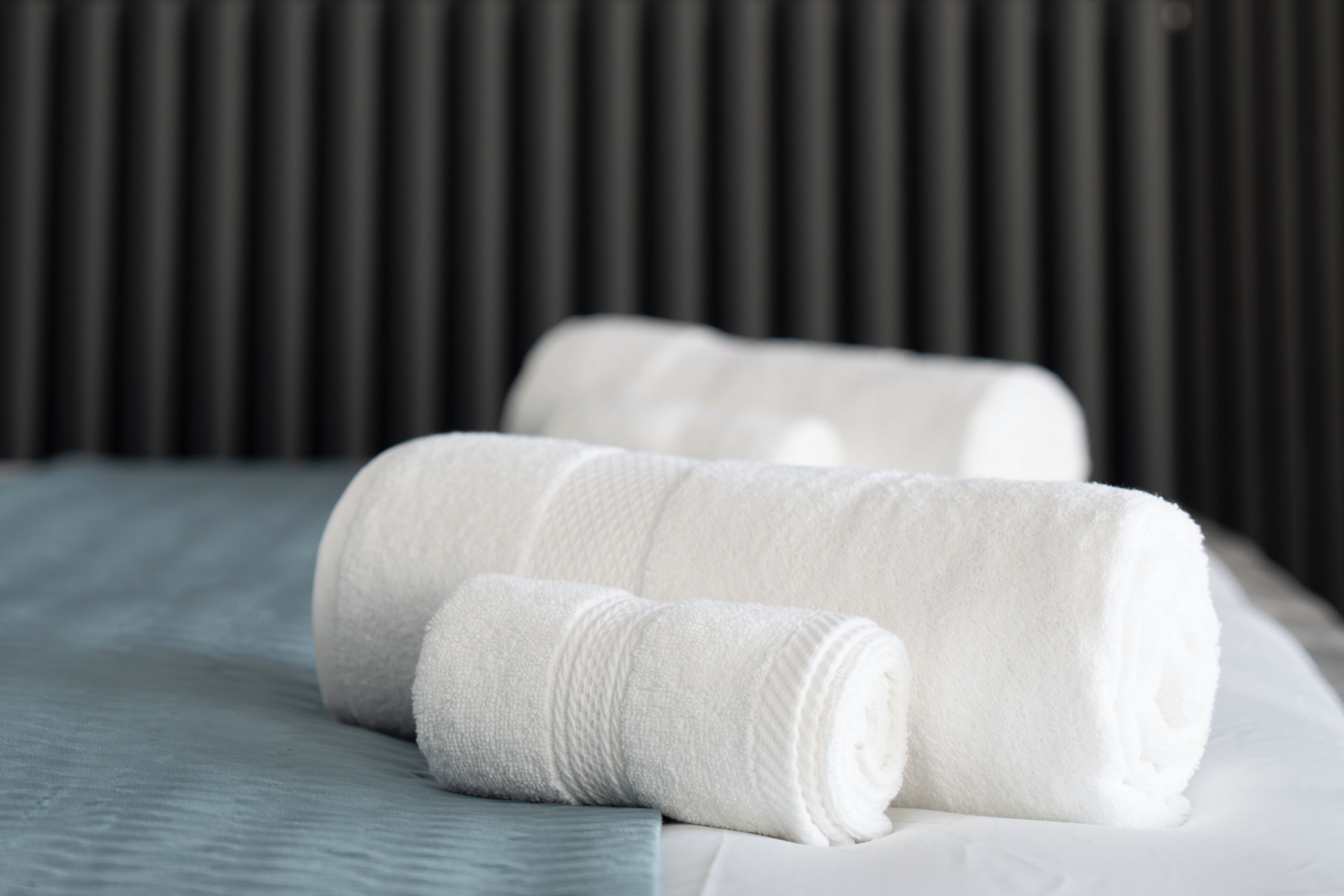 A neatly made bed with two rolled white towels and a blue bedspread.