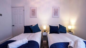 A hotel room with two beds, each with a blue blanket and pillows, a white door, and two bedside lamps.