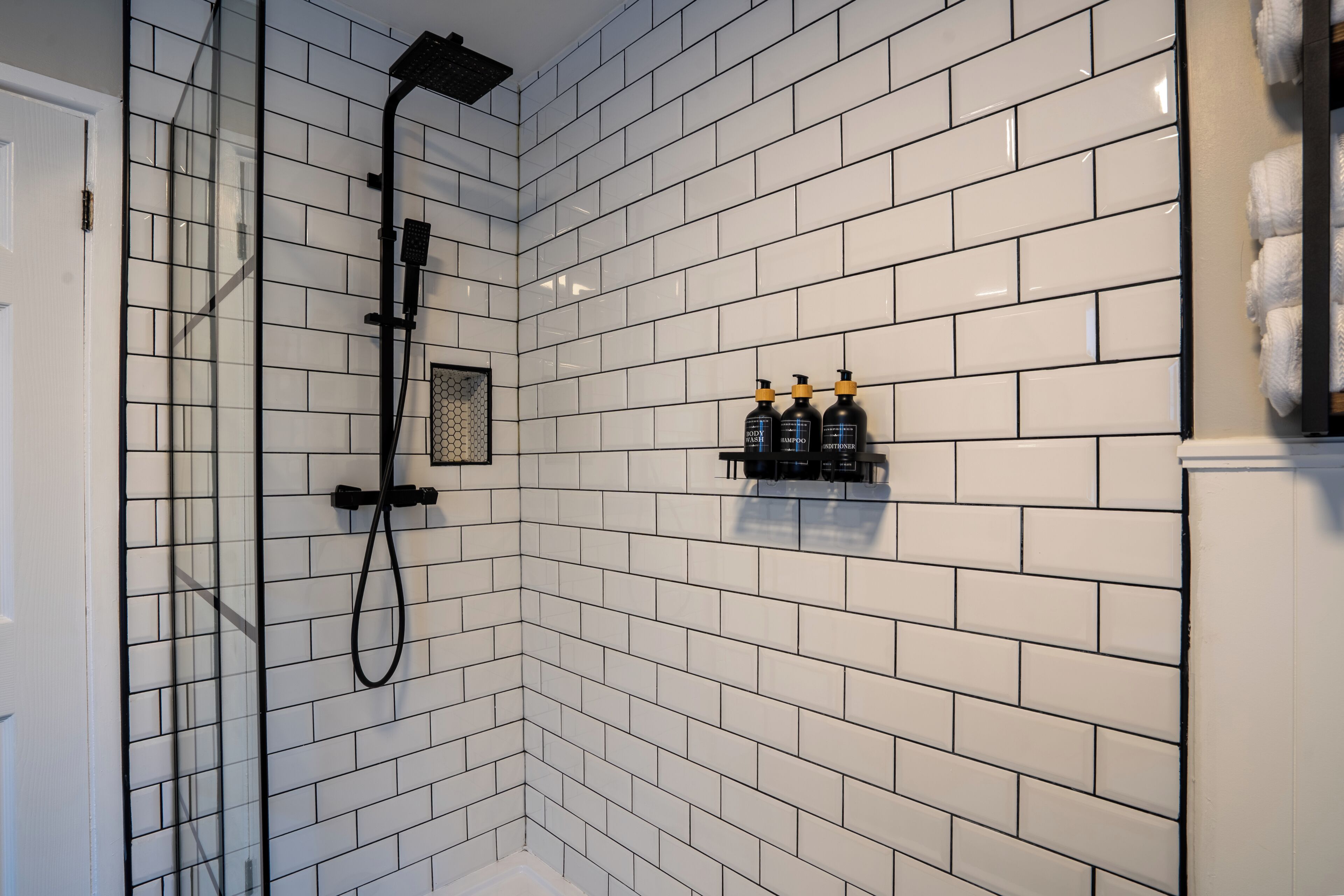 A bathroom with white subway tiles, a glass shower enclosure, and a shelf with toiletries.