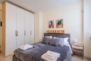 A bedroom with a bed, a wardrobe, a nightstand, and two abstract paintings on the wall.