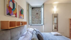 Une chambre à coucher avec un lit, une fenêtre, un mur en pierre et des œuvres d’art accrochées au mur.