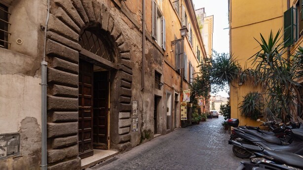 Una estrecha calle empedrada flanqueada por edificios históricos, con una gran puerta de madera y una motocicleta estacionada a la derecha.