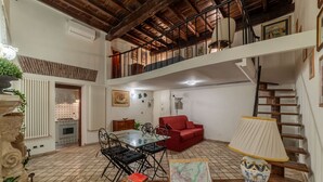 Amplia sala de estar tipo loft con mesa de comedor, sofá rojo y una escalera que conduce a un nivel superior.
