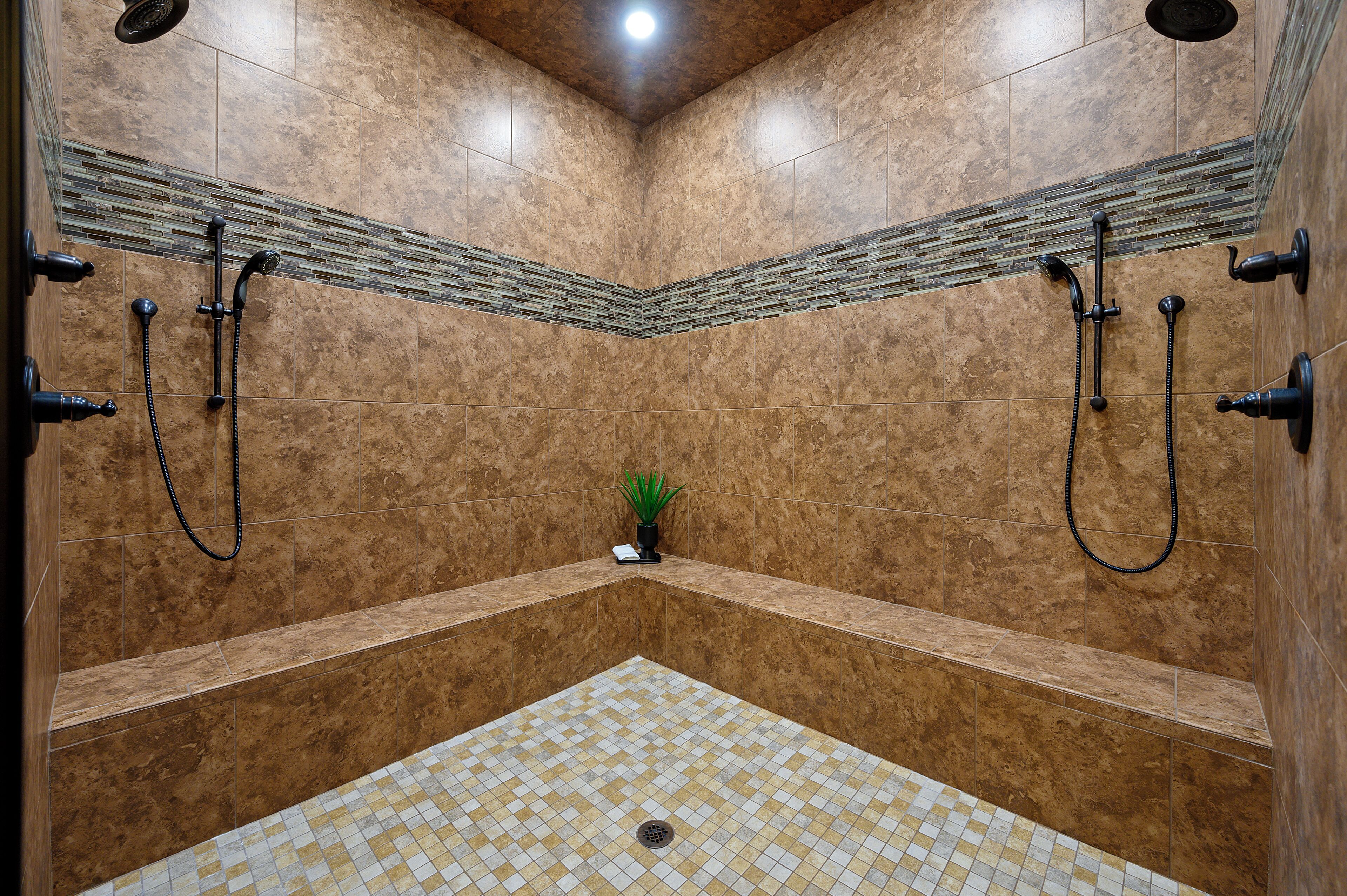 A shower area with tiled walls and floor, a small plant, and a ceiling light.
